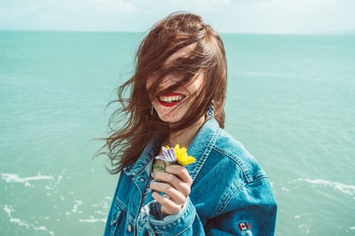 面带微笑的女人在海的前面拿着黄色的花